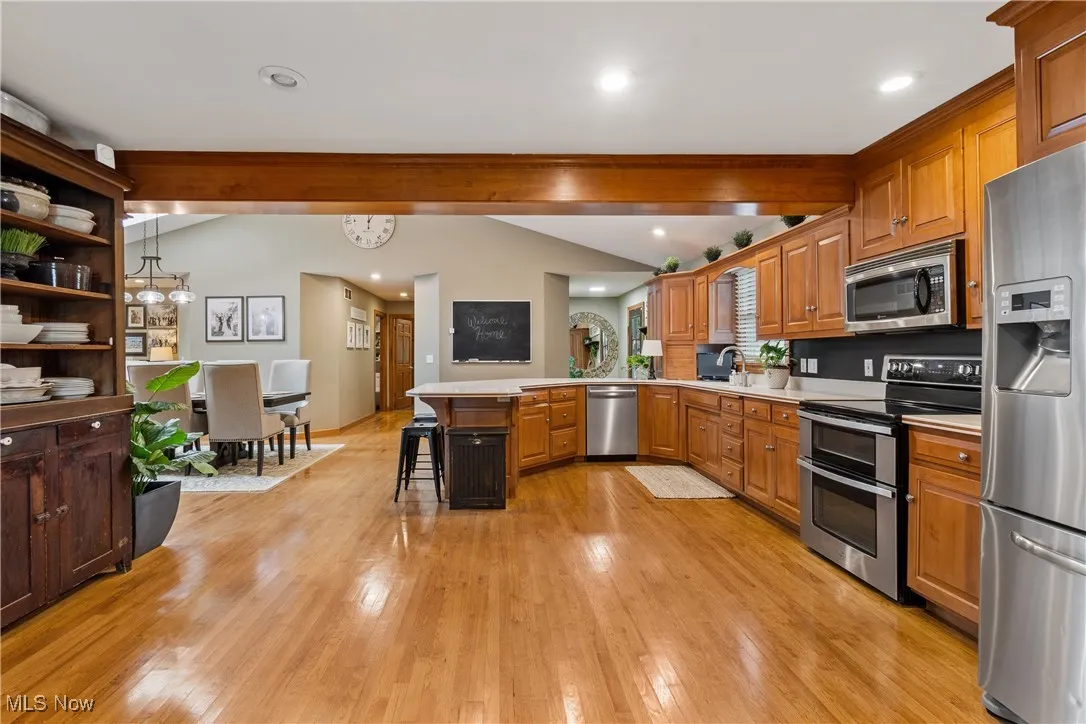 Kitchen with a peninsula, stainless steel appliances, light countertops, light wood finished floors, and a kitchen bar
