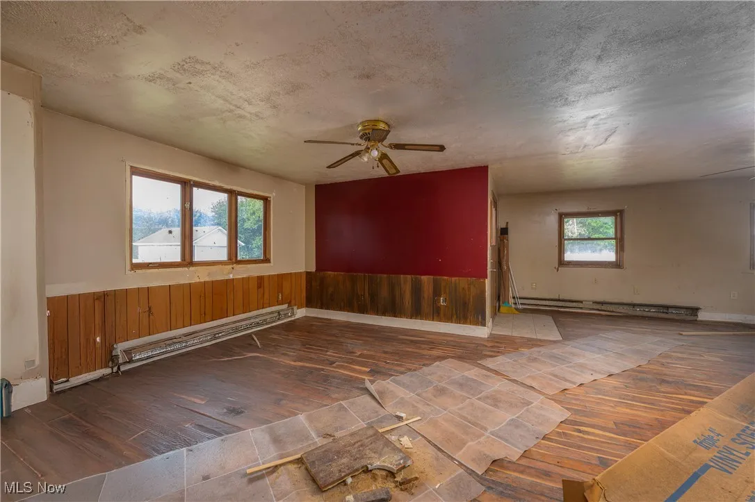 Spare room featuring hardwood / wood-style floors, a ceiling fan, a wainscoted wall, baseboard heating, and wooden walls
