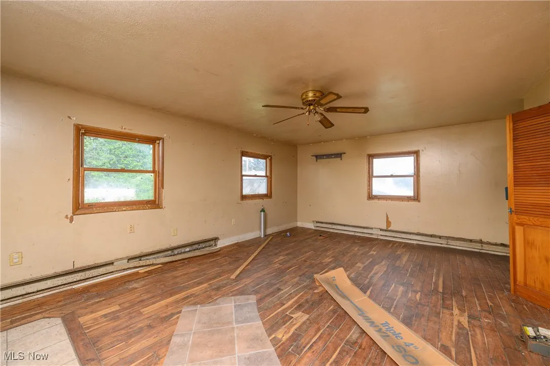 Unfurnished room with hardwood / wood-style flooring, a baseboard heating unit, and a ceiling fan