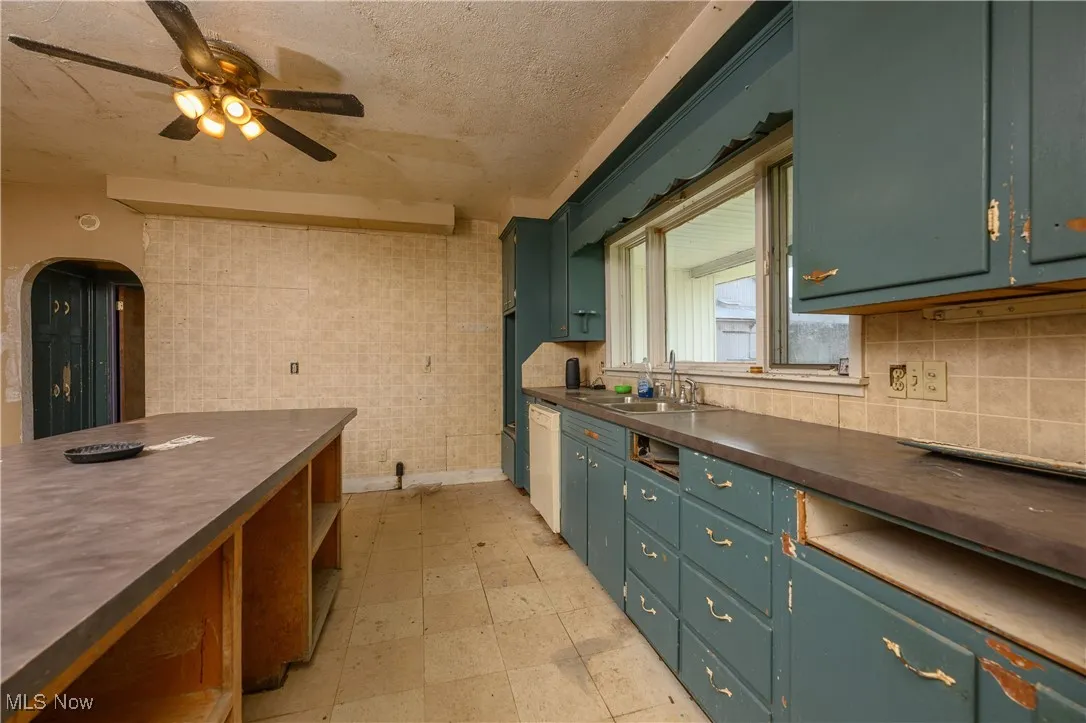 Kitchen featuring dark countertops, ceiling fan, arched walkways, tile walls, and dishwasher