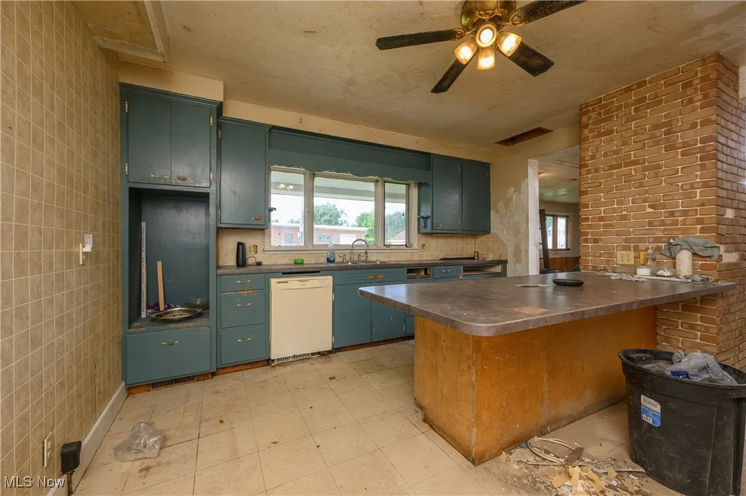 Kitchen with stainless steel countertops, white dishwasher, a peninsula, ceiling fan, and light flooring