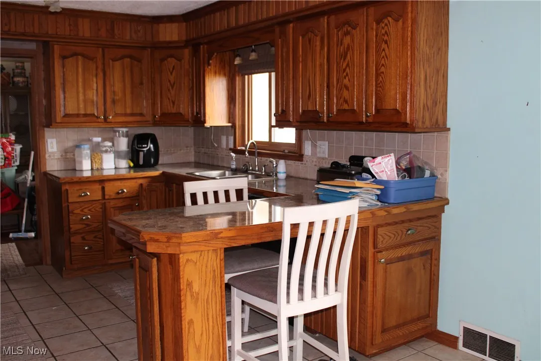 Kitchen with backsplash, light tile patterned floors, and brown cabinetry