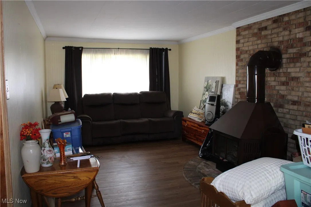 Living area with wood finished floors, ornamental molding, and a wood stove