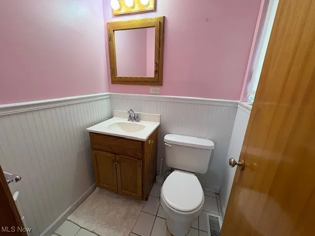 Half bathroom with wainscoting, vanity, and tile patterned flooring