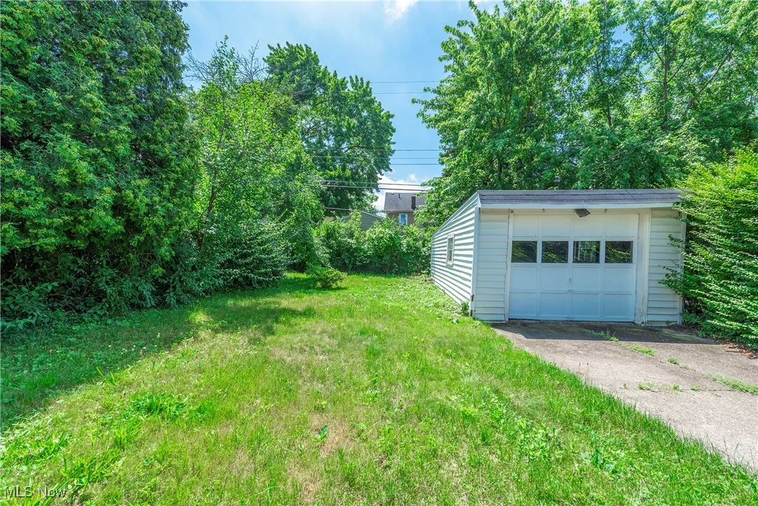 View of grassy yard with an outdoor structure, driveway, and a garage