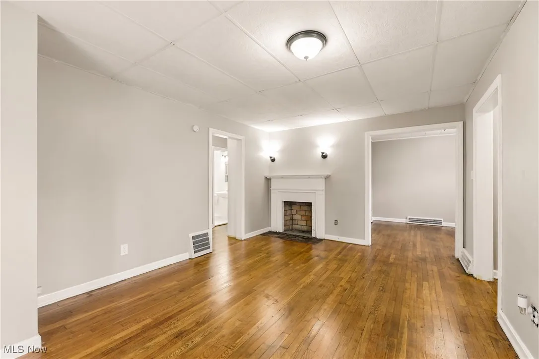 Unfurnished living room with hardwood / wood-style flooring, a fireplace with flush hearth, and a drop ceiling