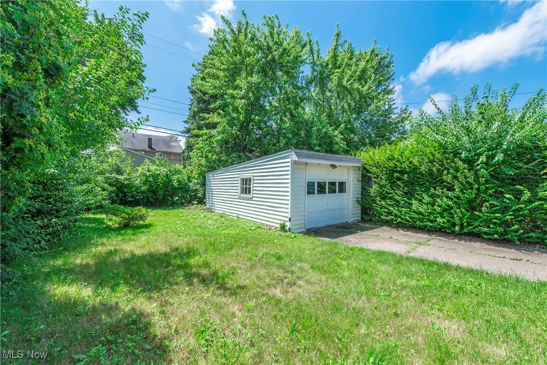 View of grassy yard featuring an outbuilding, a garage, and driveway