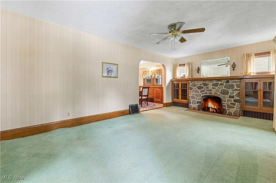 Unfurnished living room featuring arched walkways, a ceiling fan, carpet, a fireplace, and a textured ceiling