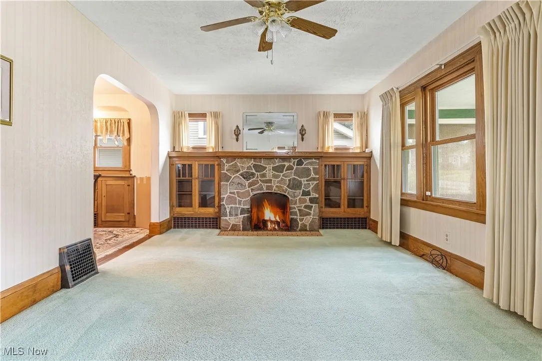 Unfurnished living room with carpet, wallpapered walls, ceiling fan, a fireplace, and healthy amount of natural light