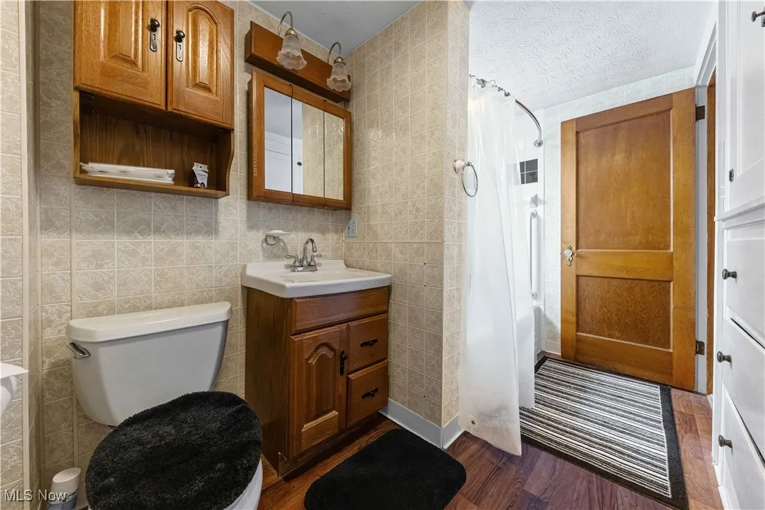 Bathroom with wood finished floors, vanity, tile walls, and a shower with curtain