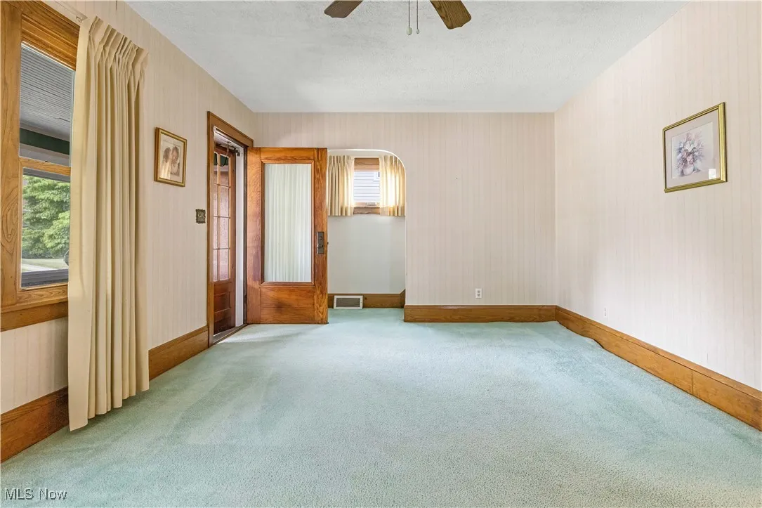 Carpeted spare room with ceiling fan, arched walkways, a textured ceiling, and wallpapered walls