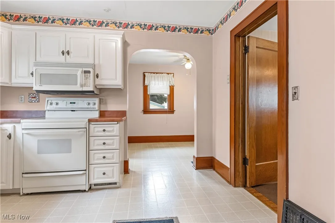 Kitchen featuring white appliances, white cabinets, arched walkways, a ceiling fan, and light countertops