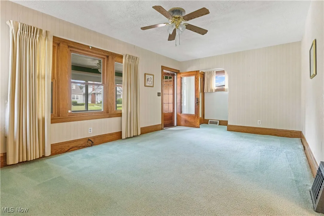 Unfurnished room featuring carpet floors, ceiling fan, a textured ceiling, wallpapered walls, and arched walkways