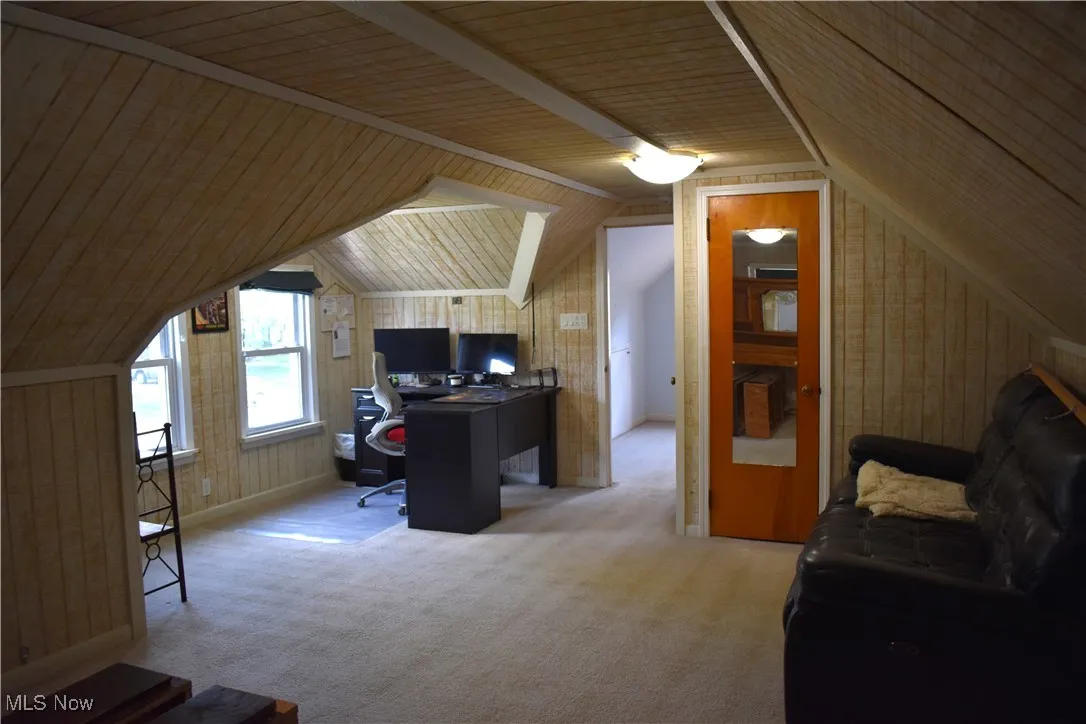 Bedroom with light colored carpet, vaulted ceiling, and wood walls