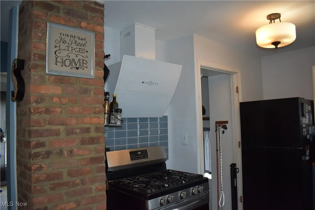 Kitchen with stainless steel range with gas cooktop, freestanding refrigerator, extractor fan, and decorative backsplash