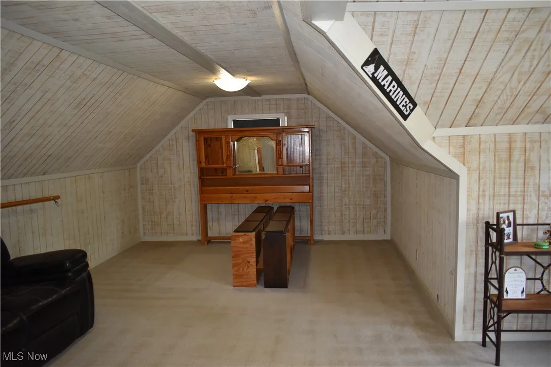Bedroom with lofted ceiling, carpet, and wood walls