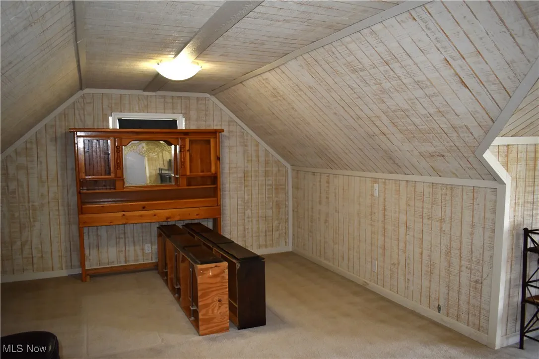 Bedroom with lofted ceiling, carpet, and wood walls