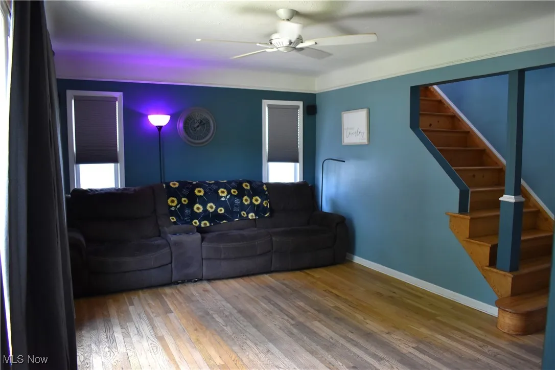 Living room featuring ceiling fan, wood finished floors, and stairway