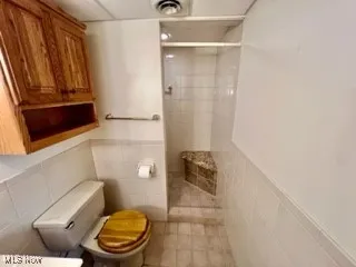 Full bath featuring a tile shower, tile walls, a wainscoted wall, and tile patterned floors