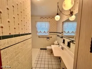 Full bathroom featuring plenty of natural light, tile patterned floors, vanity, and tile walls