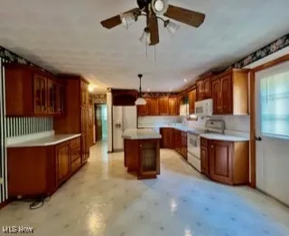 Kitchen with a center island, glass insert cabinets, white appliances, hanging light fixtures, and a ceiling fan