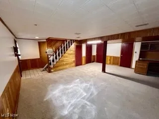 Finished below grade area featuring wooden walls, stairway, and carpet