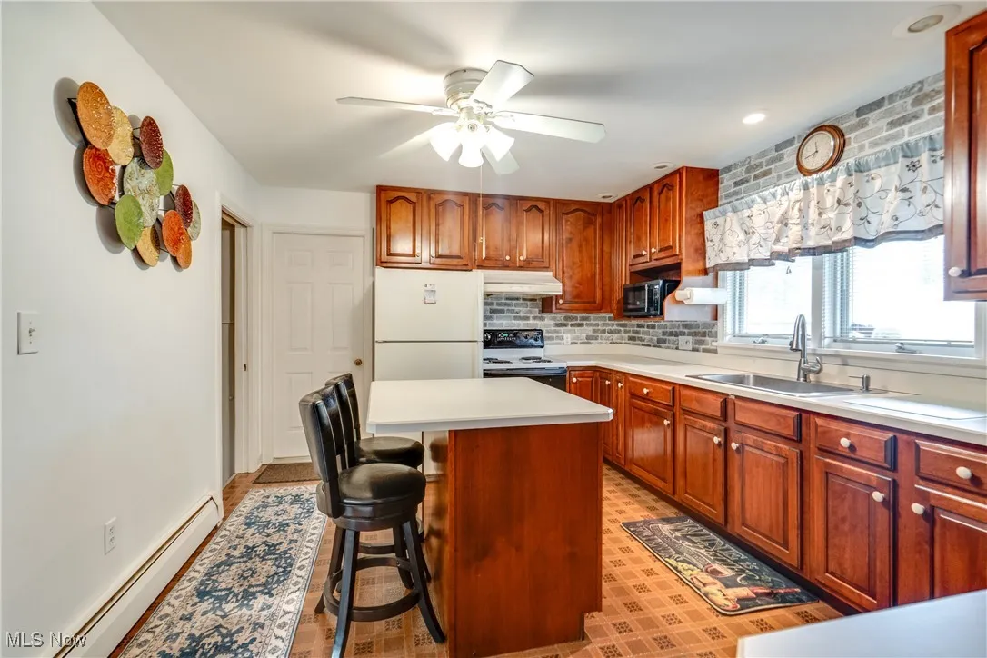 Kitchen featuring a baseboard radiator, ceiling fan, white appliances, a kitchen bar, and light countertops