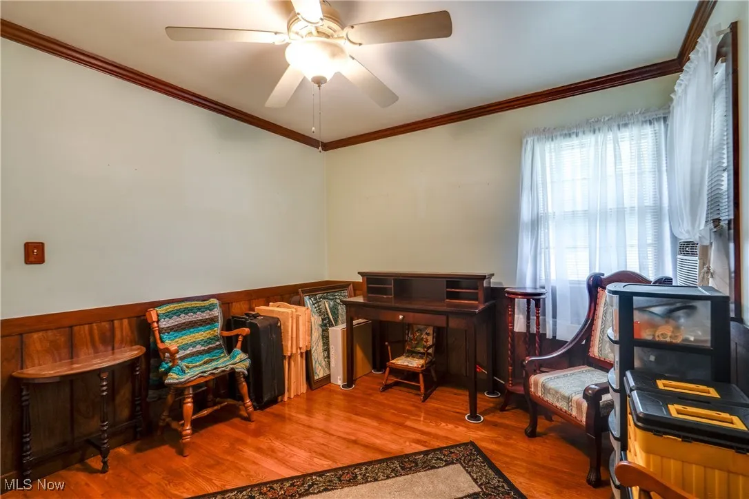 Office with wood finished floors, a wainscoted wall, ornamental molding, a ceiling fan, and wooden walls