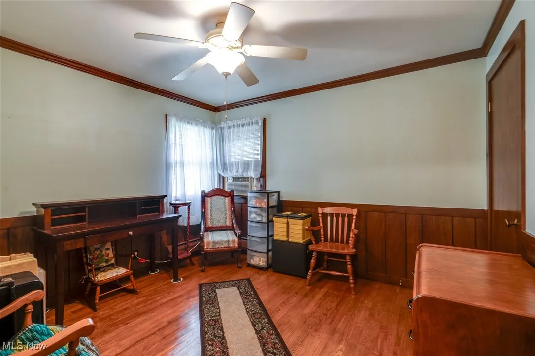 Office space featuring a ceiling fan, wood finished floors, a wainscoted wall, and crown molding