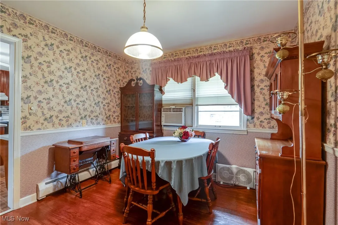 Dining area with wallpapered walls, wood finished floors, a baseboard heating unit, and cooling unit