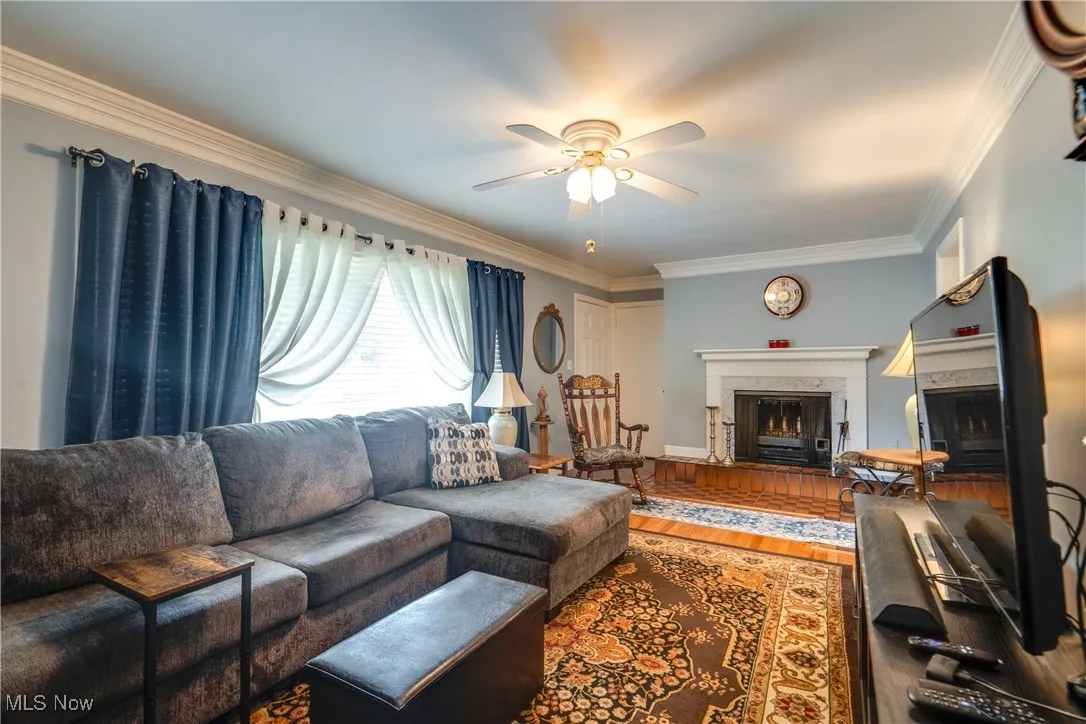 Living area with a fireplace, a ceiling fan, ornamental molding, and wood finished floors