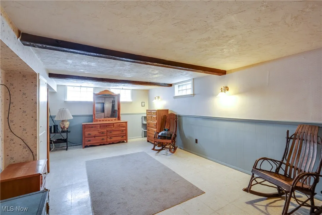 Sitting room featuring tile patterned floors, beamed ceiling, a wainscoted wall, and a textured ceiling