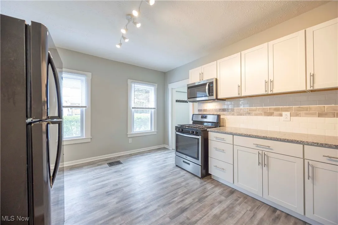 Kitchen with stainless steel appliances, tasteful backsplash, white cabinets, and light stone countertops