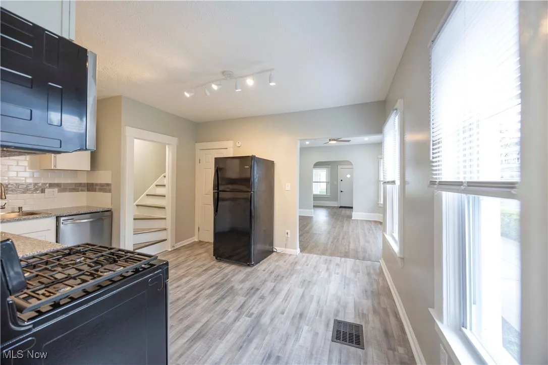Kitchen with black appliances, arched walkways, decorative backsplash, light stone counters, and light wood-type flooring
