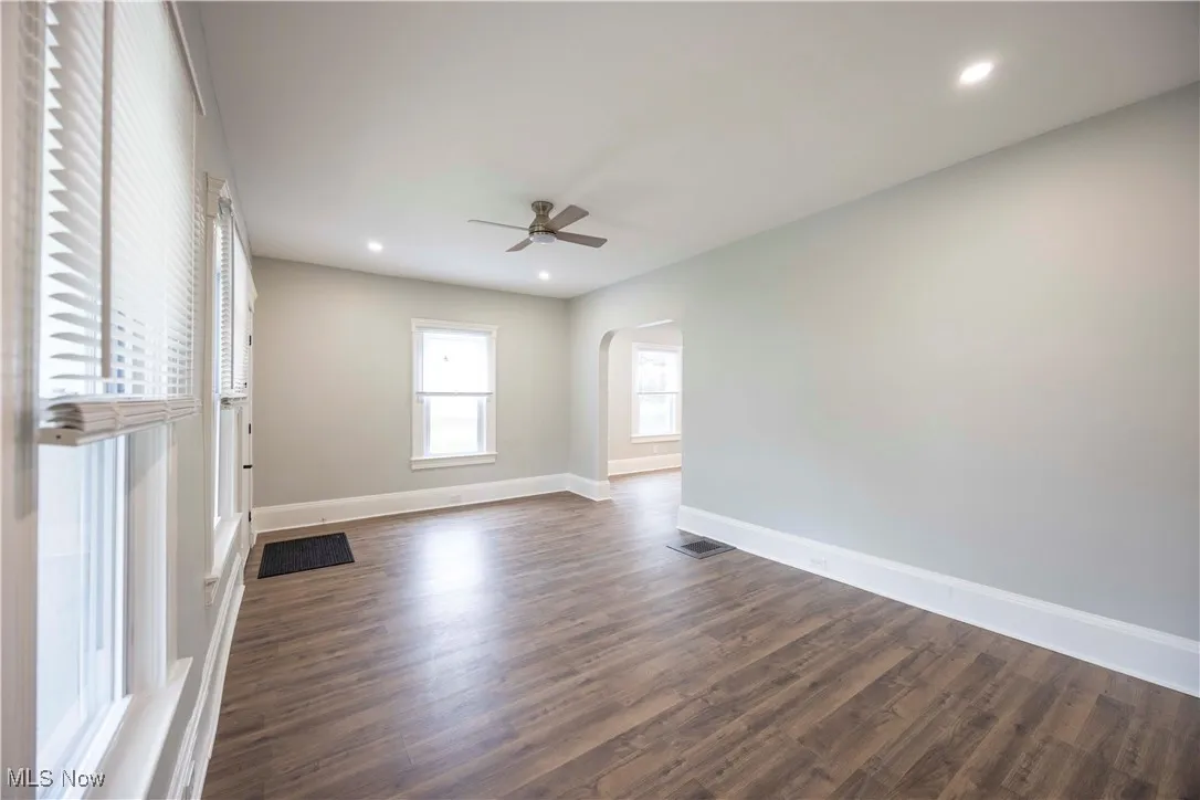 Unfurnished room featuring arched walkways, a ceiling fan, dark wood-type flooring, and recessed lighting