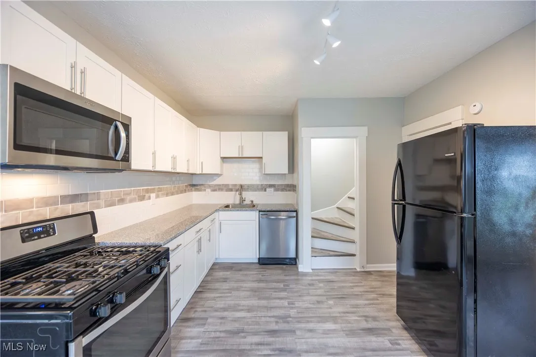 Kitchen featuring stainless steel appliances, white cabinets, tasteful backsplash, and light wood-style floors
