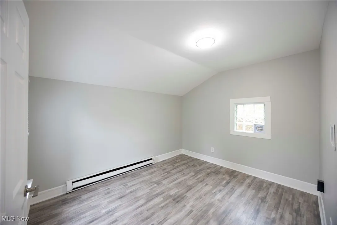 Bonus room with a baseboard heating unit, lofted ceiling, and wood finished floors