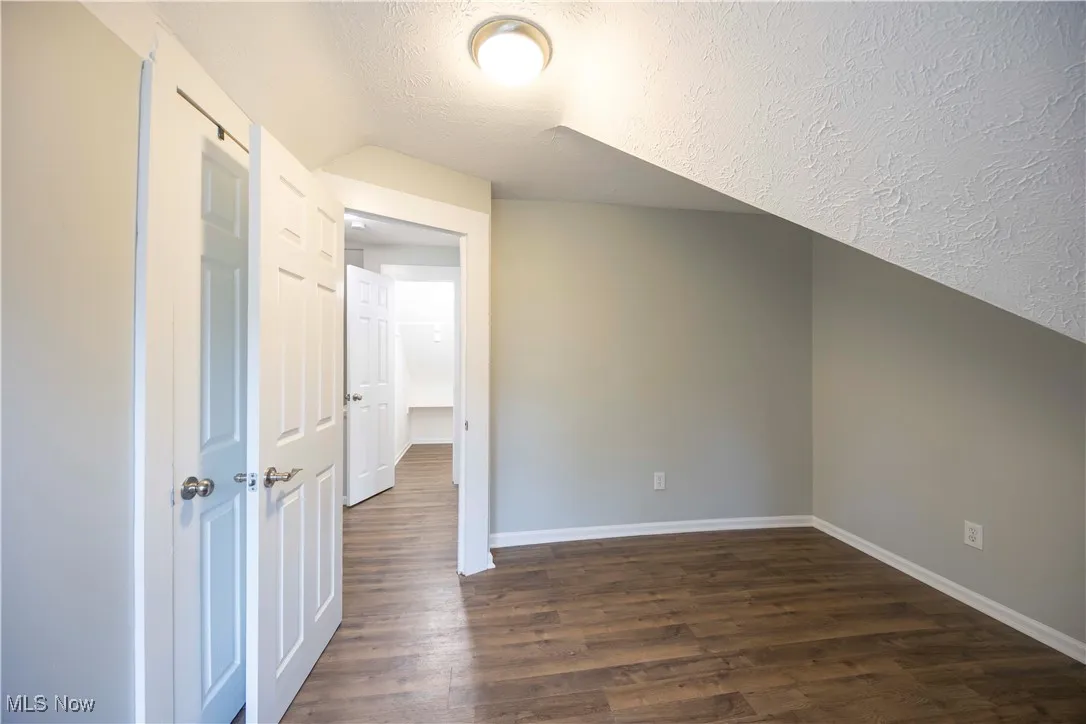 Additional living space with dark wood finished floors, lofted ceiling, and a textured ceiling