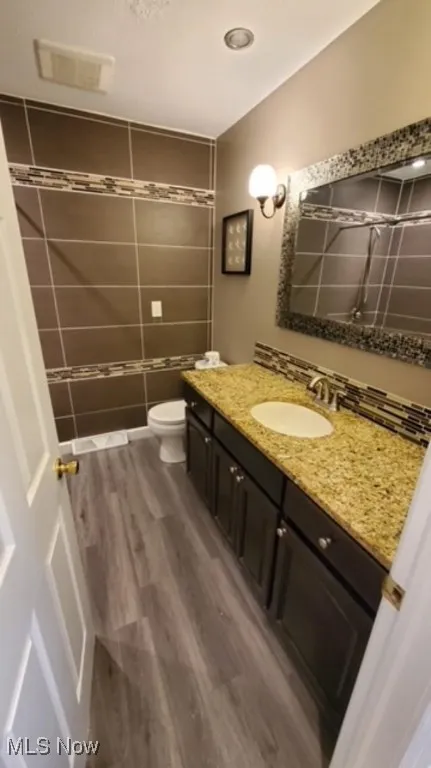 Full bathroom featuring vanity, wood finished floors, a shower, and tile walls