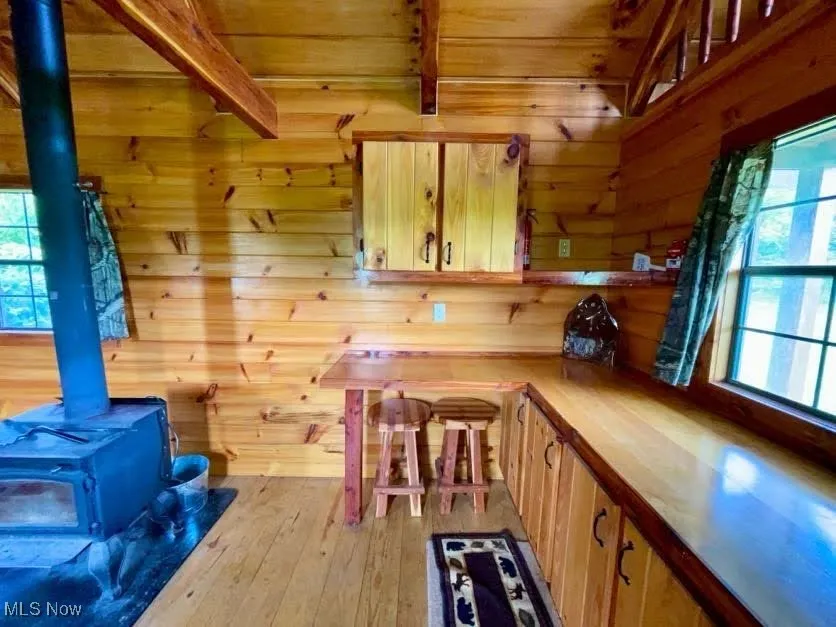 Dining area with a wood stove, plenty of natural light, wooden walls, wood-type flooring, and a wood ceiling with exposed beams