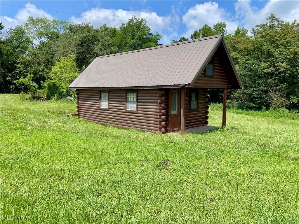 View of side of property featuring log exterior, an outbuilding, a metal roof, and a lawn