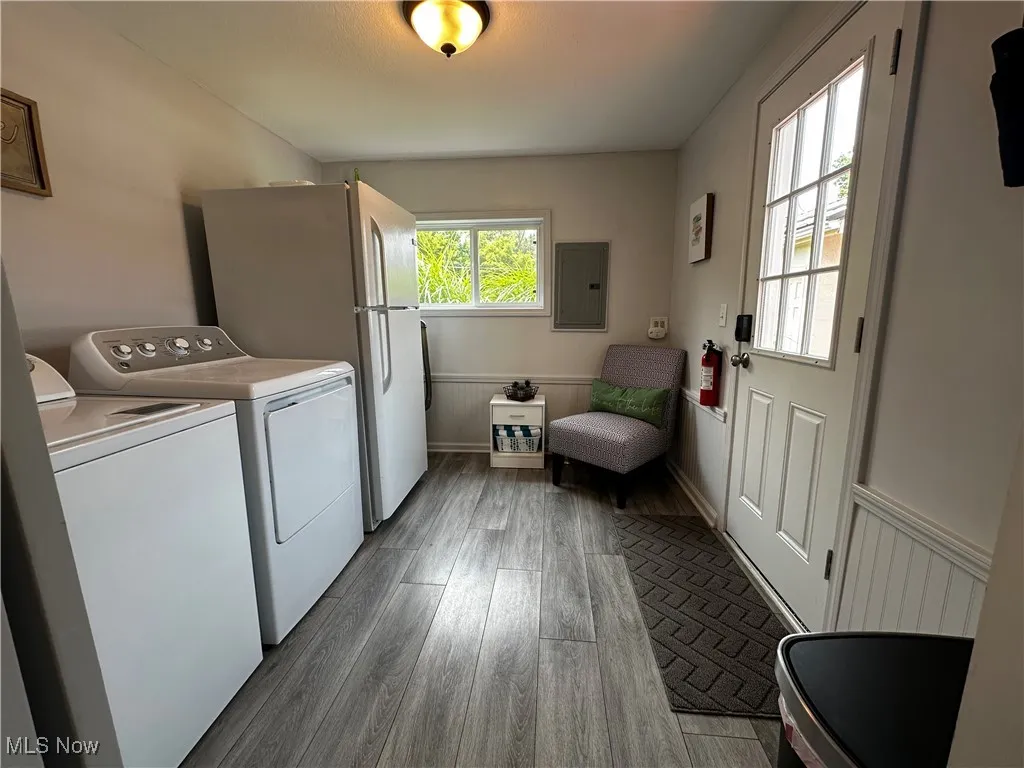 Washroom featuring dark wood-type flooring, washer and dryer, electric panel, and a wainscoted wall