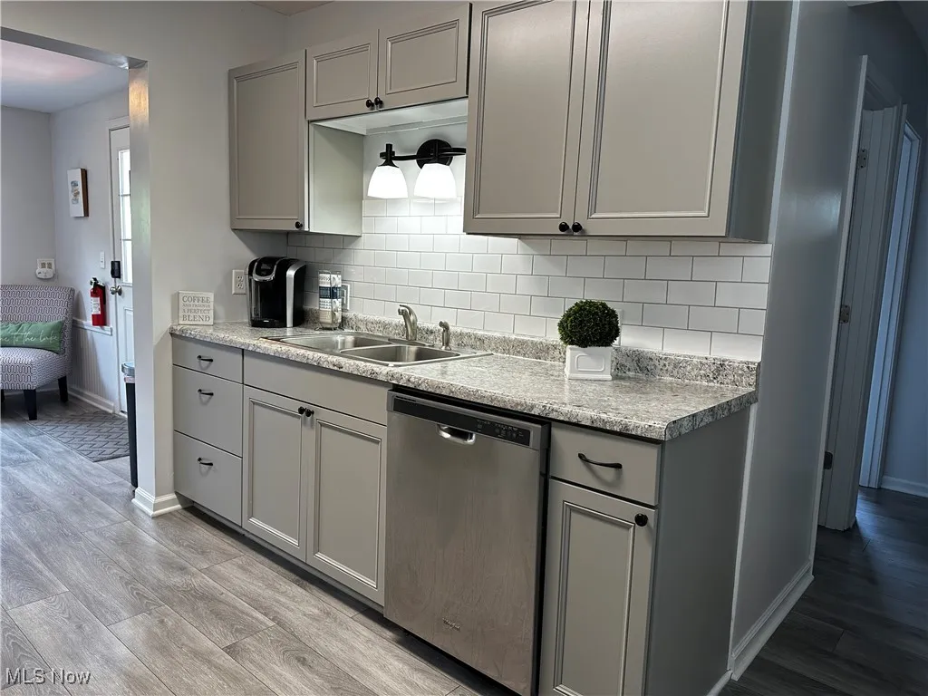 Kitchen with gray cabinetry, dishwasher, light wood finished floors, and tasteful backsplash