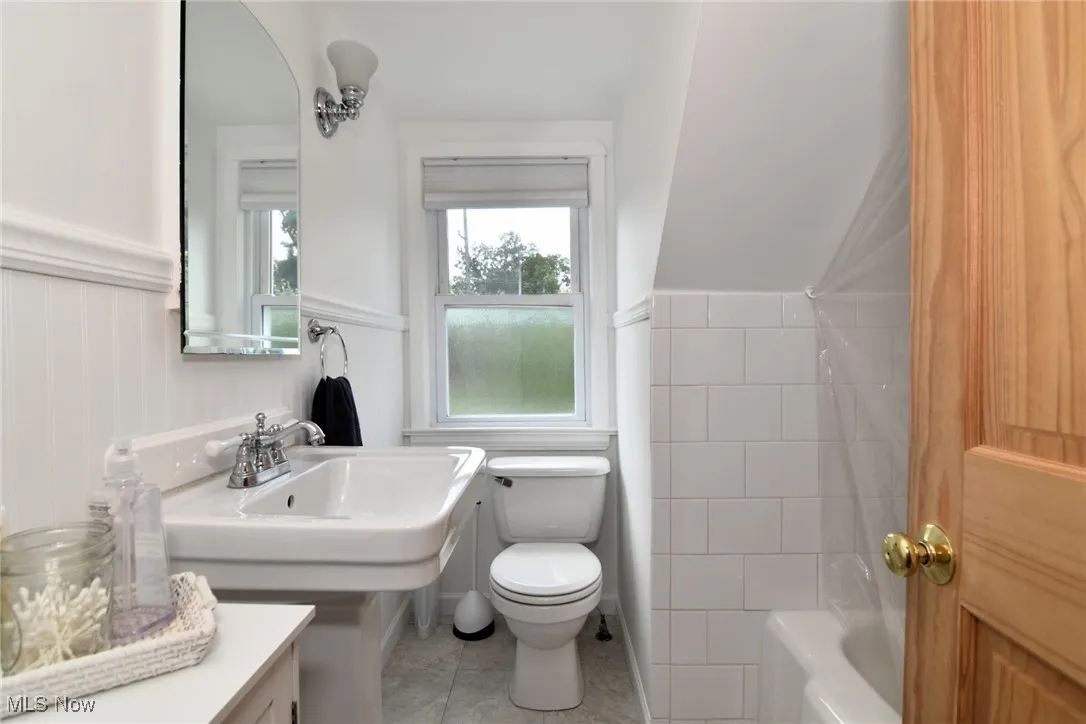 Full bath featuring wainscoting, tile patterned flooring, tile walls, and washtub / shower combination