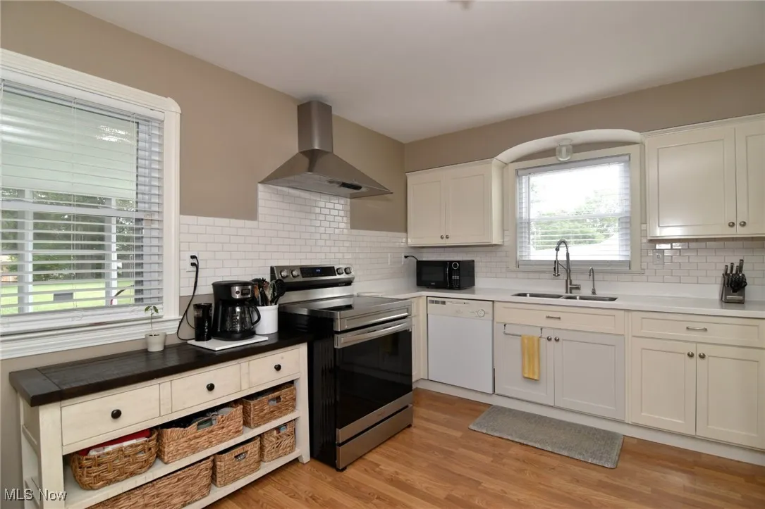 Kitchen with stainless steel electric range oven, wall chimney exhaust hood, dishwasher, and white cabinetry
