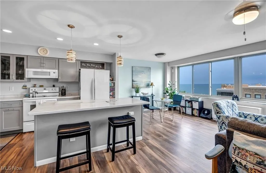 Kitchen featuring white appliances, gray cabinetry, light countertops, a kitchen breakfast bar, and glass insert cabinets