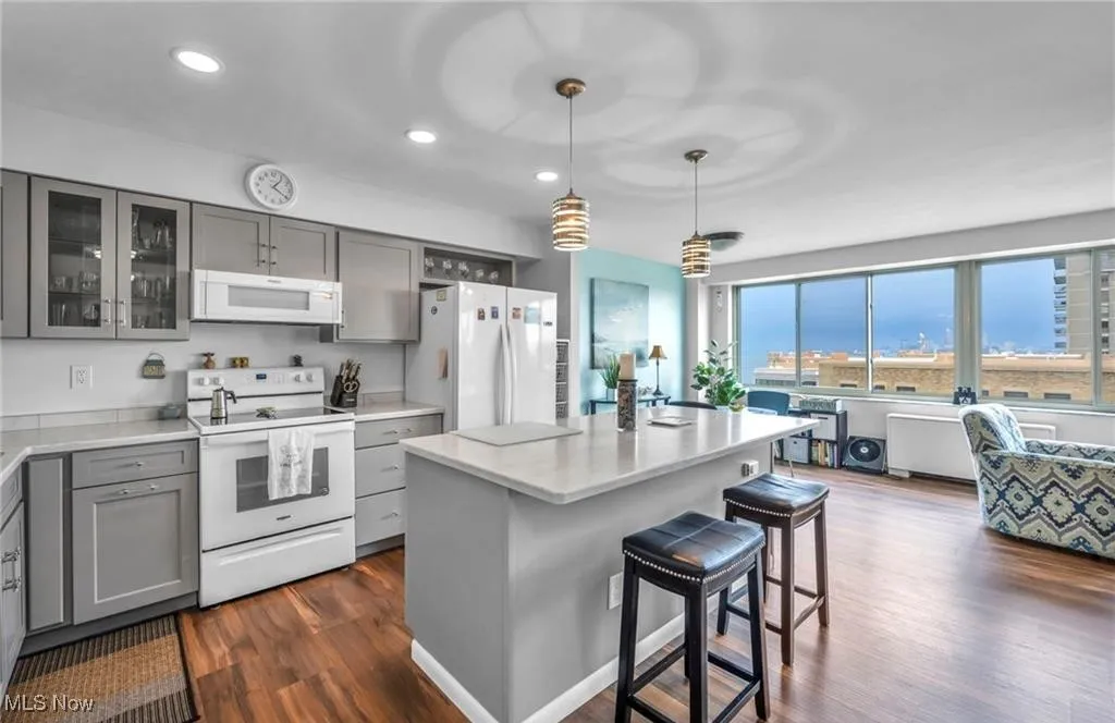 Kitchen featuring gray cabinets, white appliances, a breakfast bar, dark wood style floors, and light countertops