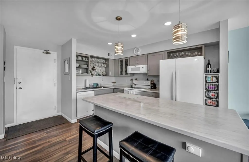 Kitchen with white appliances, light countertops, glass insert cabinets, dark wood style flooring, and a breakfast bar