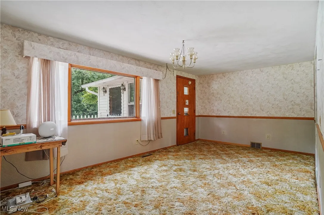 Spare room featuring a chandelier, wallpapered walls, and carpet floors