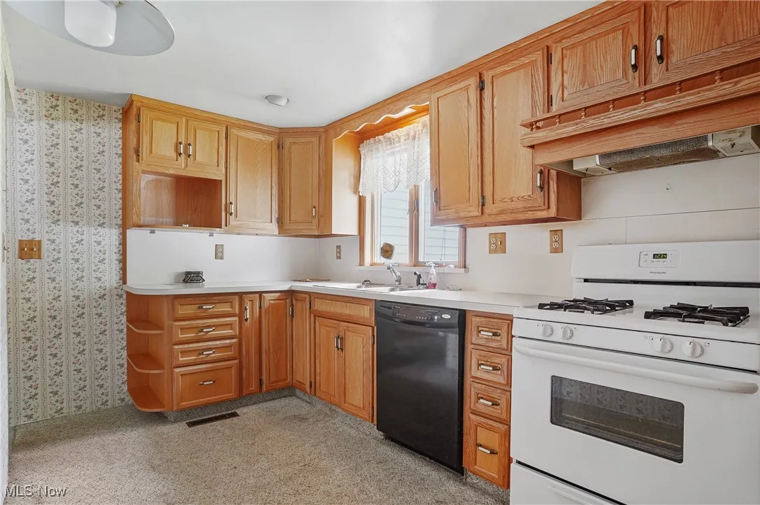 Kitchen featuring white gas range, wallpapered walls, dishwasher, light countertops, and under cabinet range hood